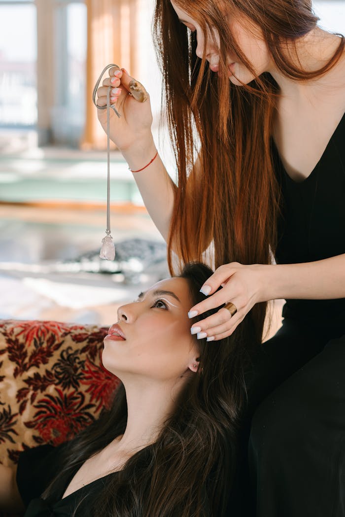 about-04 Two women engage in mindfulness and healing with a crystal pendulum indoors.