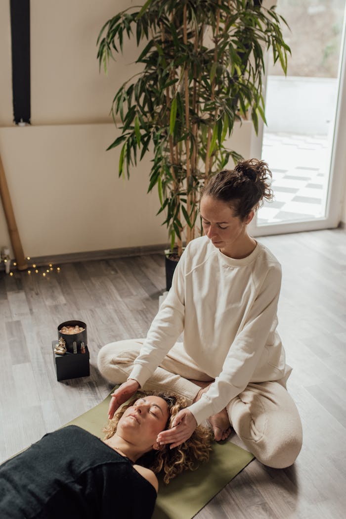 A calming scene depicting a woman practicing Reiki therapy on another woman lying on a yoga mat indoors.